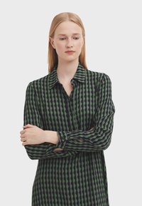 Long-sleeve button-up shirt, featuring a diamond pattern in green and navy, with a collar and soft texture.
