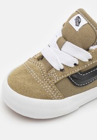 Zapatillas de lona marrón claro con cordones blancos, detalles en negro y ante texturizado. Cuenta con una puntera redonda y una suela de goma blanca con agarre estampado.