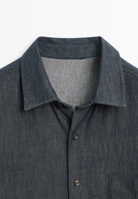 Dunkelblaues Jeanshemd mit strukturiertem Kragen, fünf Knöpfen auf der Vorderseite und einer Brusttasche. Der Stoff hat ein dezentes strukturiertes Muster.