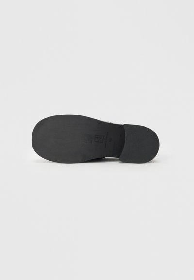 Black shoe sole with a smooth, rubbery texture and a rounded shape. Features minimal markings and a slight curvature at the heel.