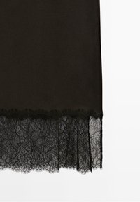Panneau en tissu noir avec une large bordure en dentelle présentant des motifs floraux le long du bord inférieur sur fond blanc.