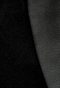 Zwart textiel met een gestructureerd oppervlak gecombineerd met een gladde, donkergrijze gestreepte stof, wat een contrast in afwerking en kleur laat zien.