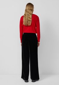 Rode lange mouwen top gecombineerd met zwarte fluwelen broek met wijde pijpen. Gladde textuur en ontspannen pasvorm met een elastische tailleband.