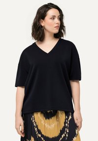 Černé oversized tričko s v-výstřihem vyrobené z měkké látky, s krátkými rukávy a uvolněným střihem, v kombinaci s plisovanou sukní s potiskem.