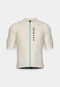 Maillot de cyclisme à manches courtes en beige clair avec une fermeture éclair bleue à l'avant, comportant un logo vertical noir "OAKLEY" et une bordure élastique pour un ajustement sécurisé.