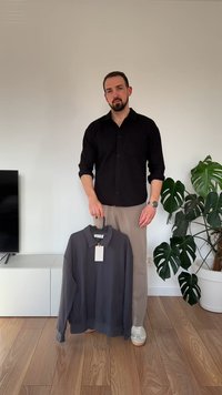 Pánská polo košile s dlouhým rukávem v tmavě šedé barvě, kterou drží člověk. Košile má límec, visačku a pružné manžety. Hladký materiál a neformální design.