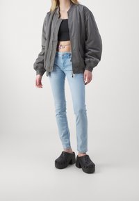Šedá bomber bunda, černý crop top, světle modré skinny džíny a černé platformové dřeváky s ventilačními otvory. Jednoduchý, moderní ležérní outfit.