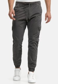Gray cargo joggers with elastic cuffs, drawstring waist, side pockets, and smooth fabric texture, paired with white sneakers.