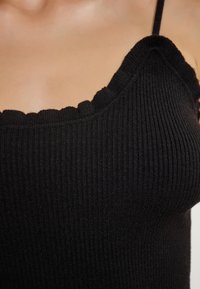 Musta ribbed-hihaton paita, jossa on aaltoileva pääntie ja ohuet hihnat. Kangas näyttää pehmeältä ja siinä on teksturoitu pinta.