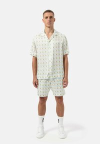 Korte mouwen, shirt met kraag en bijpassende shorts in lichtgroen met een bloemenpatroon. Lichtgewicht stof, casual pasvorm, gedragen met witte sneakers.