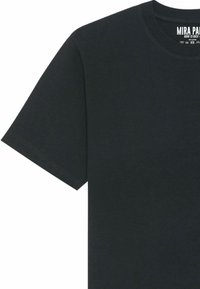 T-shirt noir en coton avec des manches courtes, col rond, et une étiquette imprimée avec "MIRA PA" et des instructions d'entretien à l'intérieur de l'encolure.