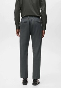 Donkergrijze broek met een elastische tailleband, voorzien van zijzakken en een getailleerde pasvorm, gecombineerd met zwarte schoenen en een overhemd met lange mouwen.