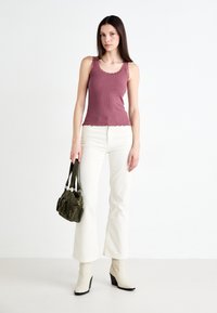 Top in mussola a coste color malva con pizzo, abbinato a pantaloni bianchi a zampa d'elefante. Porta una borsa a tracolla in corduroy verde. Stivaletti bianchi alla caviglia con tacco a blocco.