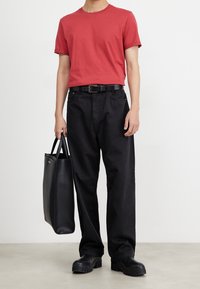 Camiseta roja de manga corta, pantalones sueltos negros, cinturón negro, botas gruesas negras y una bolsa tote negra con asas.