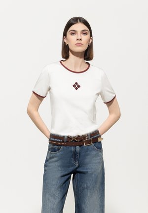 White cotton t-shirt with burgundy trim and central floral embroidery. Paired with high-waisted, light blue denim jeans and a brown belt.