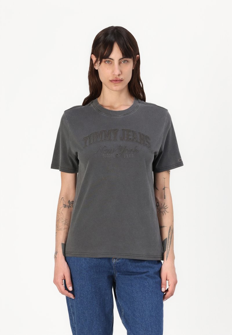 Graues Baumwoll-T-Shirt mit Rundhalsausschnitt und kurzen Ärmeln, mit eingeprägtem "TOMMY JEANS New York seit 1985"-Text auf der Vorderseite.
