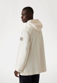 Beige hoodie met een ontspannen pasvorm, gemaakt van gladde stof. Voorzien van een logopatch op de mouw en met knopen verstelbare manchetten.