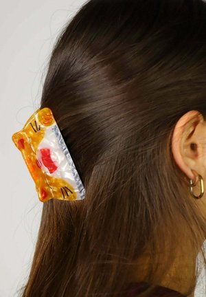 Clip de pelo de plástico con diseño de gato en tonos naranja y blanco, bordeado en gris. Forma de gancho con textura de superficie lisa y brillante.