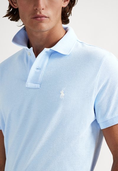 Svetlomodrá polokošeľa z textúrovanej látky, so štandardným golierom, zapínaním na dve gombíky a malým bielym logom na hrudi.