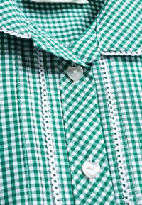 Chemise en tissu à carreaux verts et blancs avec un col chemise, ornée de boutons en forme de cœur et de délicats détails de galon blanc.