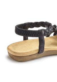 Schwarze geflochtene Riemchensandale mit einer weichen, strukturierten Fußbett und einer geschwungenen, natürlichen Sohle. Mit metallischen Akzenten an den Riemen.