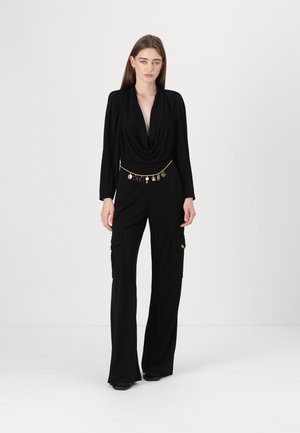 Salopette cargo nera con scollatura drappeggiata, maniche lunghe e tasche. Presenta una cintura in oro con charm decorativi. Tessuto dalla texture liscia.