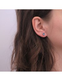 Boucle d'oreille en stud bleu rond en argent, placée sur le lobe d'une oreille. La boucle d'oreille a une surface lisse et une réflexion de lumière.