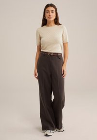 Bēšas adītas īsām piedurknēm svārki ar teksturētām punktiem, apvienoti ar augsto jostasvietu platajām tumši brūnām biksēm un brūnu jostu. Ikdienas apavi.