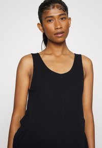 Top de tanque preto com riscas, decote redondo e alças largas. O tecido tem um acabamento texturizado, proporcionando uma silhueta ajustada.