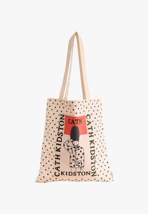 Puuvillane kott, mille hele virsiku taustal on mustad täpid ja graafiline kaitsefiguur. Esitleb nime "Cath Kidston" julgelt kirjutatud tekstiga.