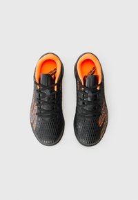 Svarta sportskor med en texturerad mesh-övre, svarta snören och ljusa orange accenter, med ett hexagonalt mönster och vadderad insida.