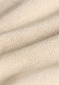 Hellbeiges Gewebe mit glatter Textur und feinem Strickmuster, das sanfte Falten und subtile Farbnuancen zeigt.