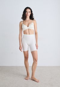 Bjela pamučna bralette i šorts visokog struka, glatke teksture, minimalistički dizajn, uskog kroja, smješteni na svjetlosivoj pozadini.