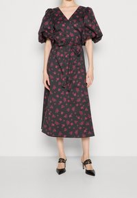Vestido cruzado negro con estampado floral, mangas cortas abullonadas, escote en V, cinturón a juego y largo midi fluido. Acentuado con pequeñas flores rosas.