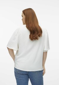 Witte, kortek mouwtop met een gestructureerde afwerking, boxy vorm en een ronde zoom, gecombineerd met blauwe denim jeans.