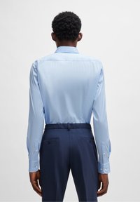 Camisa de manga larga azul claro con textura suave, que presenta una espalda con canesú y puños con botones, combinada con pantalones azul marino oscuro y una cintura clásica.