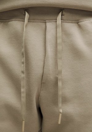 Pantalons de survêtement beiges avec un tissu texturé, une taille élastique et des cordons assortis avec des embouts en plastique. Design simple et pratique.