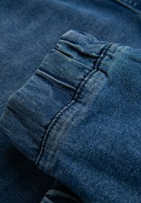 Tela de mezclilla en azul oscuro, con un detalle de puño fruncido que presenta una textura sutil, costuras visibles y un acabado suave.