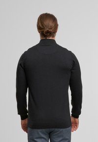 Schwarzer Strickpullover mit hohem Kragen, taillierten Bündchen und glatter Textur. Verfügt über ein rundes Detail am Nacken hinten.