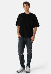 Černé oversized bavlněné tričko s krátkými rukávy, s kapsou na prsou, spárované s tmavými prodřenými džíny a stříbrnými sportovními botami.