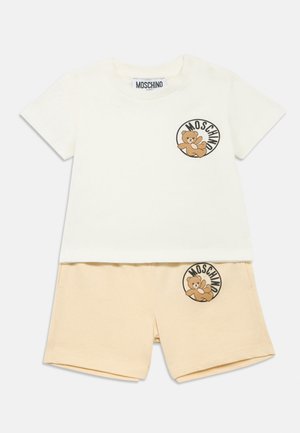 Hvit T-skjorte med korte ermer og bjørnelogo, og beige shorts med en matchende bjørnepatch. Laget av myk bomull med en avslappet passform.