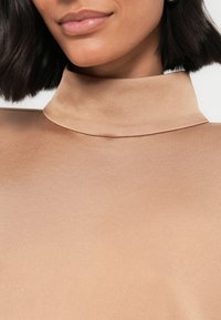 Ruskea korkea kauluksinen paita, valmistettu sileästä, satiinimaisesta kankaasta; siinä on istuva malli, jossa on vähän saumoja ja hienovarainen kiilto.