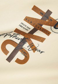Tela beige que presenta gráficos de texto en marrón y naranja, incluyendo "Crea Tu Propio Futuro" y "Ropa Auténtica" en varias fuentes y estilos.