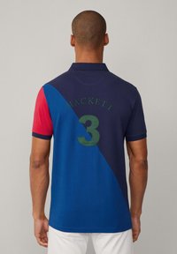 Marineblauwe en blauwe kleurblok polo met rode mouwen; voorzien van "HACKETT" en een groot groen "3" op de achterkant. Gemaakt van gladde katoen.