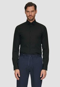 Zwarte langemouw shirt met een button-down kraag, voorzien van zes knopen aan de voorkant, gecombineerd met donkerblauwe elastische broek.