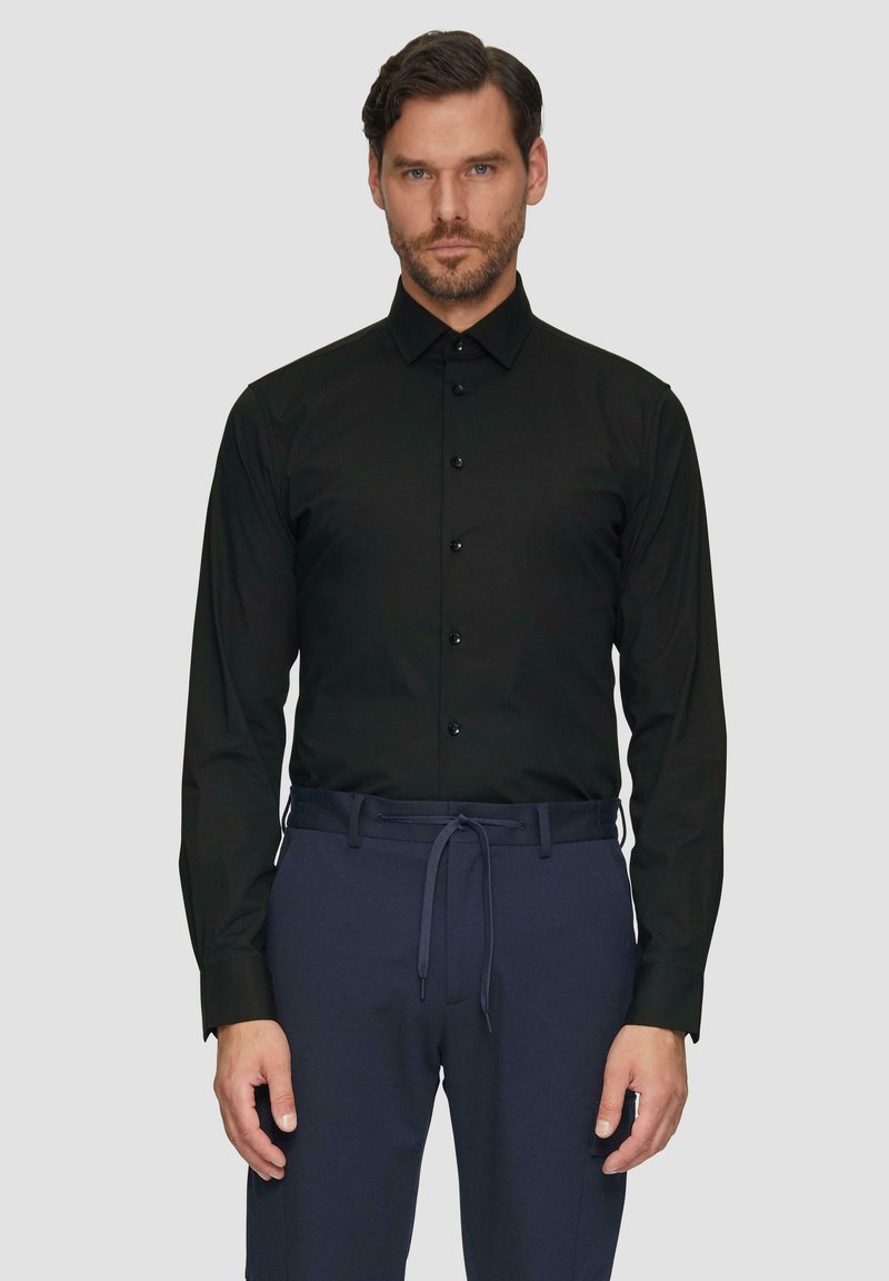 Zwarte langemouw shirt met een button-down kraag, voorzien van zes knopen aan de voorkant, gecombineerd met donkerblauwe elastische broek.
