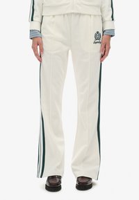 Hvide tracksuit-bukser med grønne sideløber, elastisk talje, folder og broderet logo, lavet af blødt stof. Sammen med mørke sko.