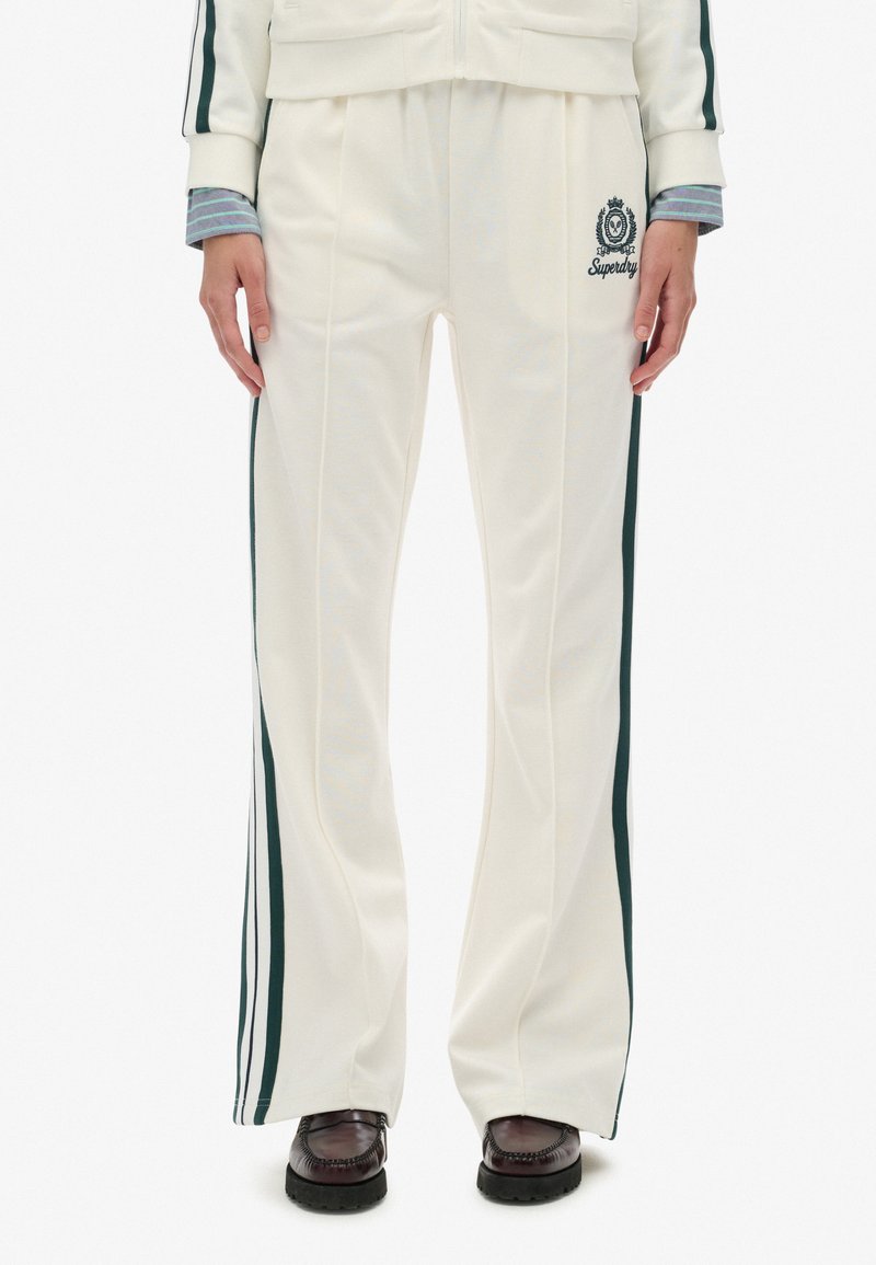 Hvide tracksuit-bukser med grønne sideløber, elastisk talje, folder og broderet logo, lavet af blødt stof. Sammen med mørke sko.