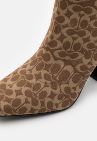 Bottine marron à motif avec un tissu doux, un bout pointu et un talon noir. Le design comprend un imprimé texturé rappelant un animal.