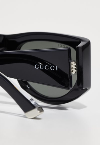 Gucci prillid ülisuurte mustade plastikkarmide, roheliste läätsede, hõbedaste seadmete aktsentide ja logoga külgedel. Läikiv viimistlus, nurkne disain.